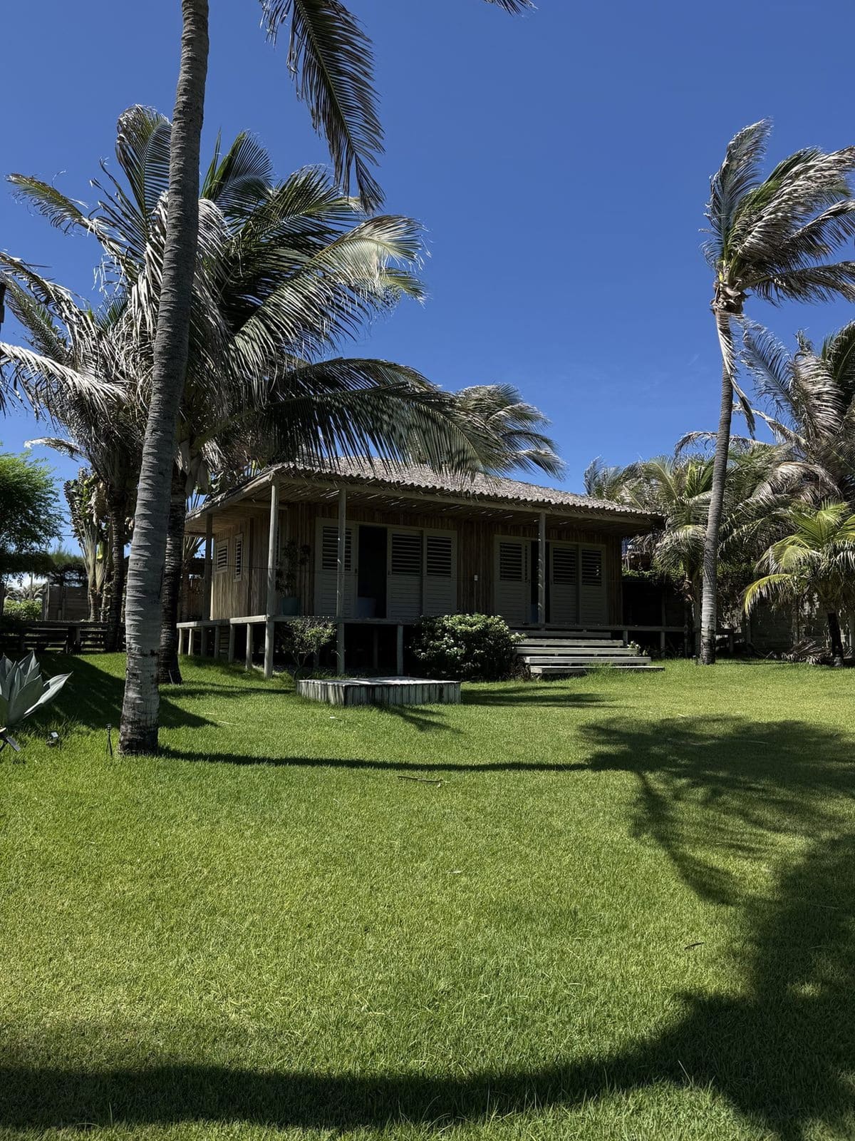 Fachada do bangalô com coqueiros e céu azul em Pontal de Maceió